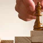 manos colocando pieza de ajedrez encima bloques de madera