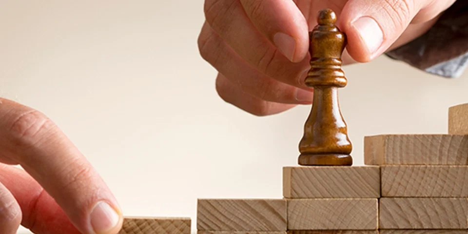 manos colocando pieza de ajedrez encima bloques de madera