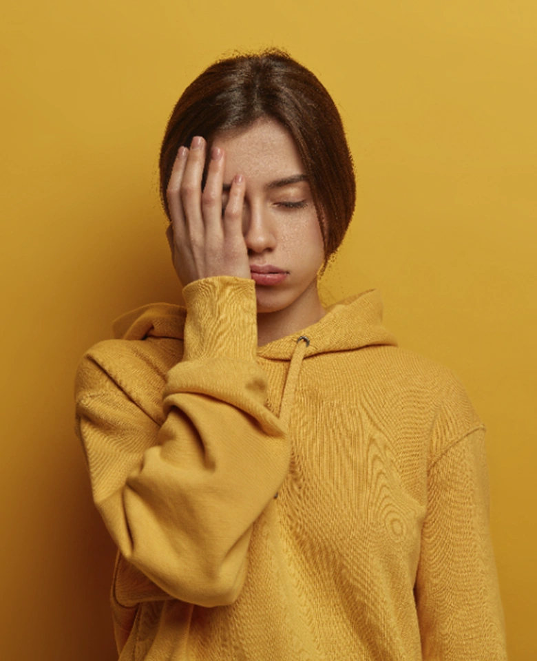 chica con sudadera naranja tapándose la cara triste